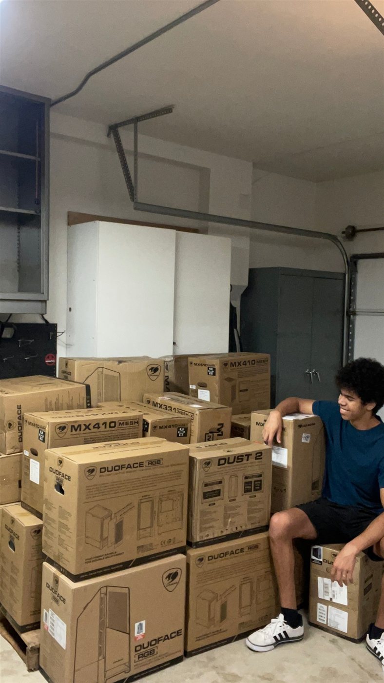 Roman in the garage with a stack of PC case boxes ready to become builds